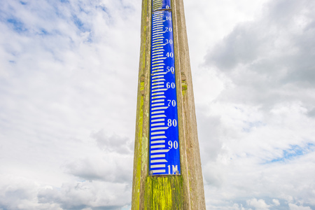Ancient tide gauge pointing into a blue cloudy skyの写真素材