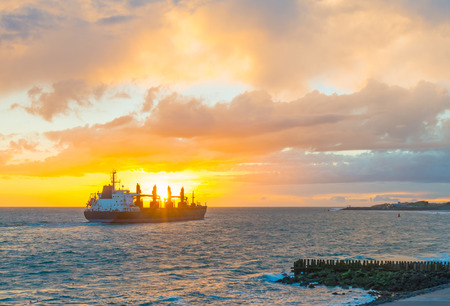 Boat sailing at sea along a dike at sunset in summerの写真素材