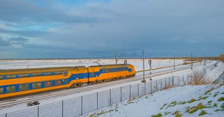 Train riding through a snowy field in sunlight in winterの写真素材