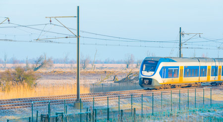 Train riding through a frozen field in sunlight in winterのeditorial素材