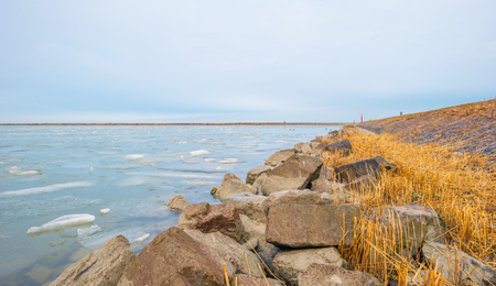 Edge of a frozen lake along a dike in winter