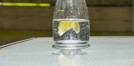 Glass pitcher with water and lemon in a sunlit rock garden at a sparkling sunny day in springの写真素材