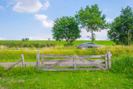 Car driving along a closed wooden fence of a pasture in the countryside in summer