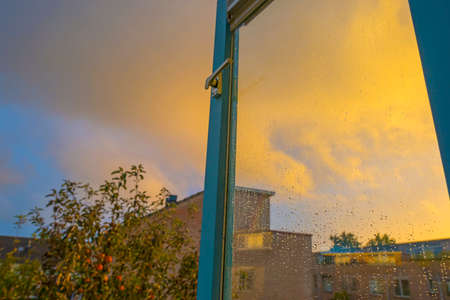 Gray yellow rain clouds over a windy rainy city causing raindrops on a window pane in autumn,...