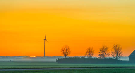 Wind turbine in a yellow sky in bright sunlight at sunrise in an early autumn morning, Almere, Flevoland, The Netherlands, November 5, 2020の写真素材