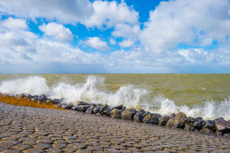 Dike of basalt stones defying a stormy lake below a blue sky and white gray clouds in spring,...