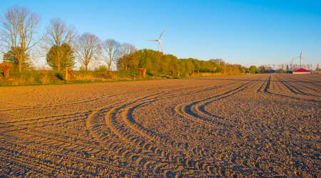 Tracks in a plowed field with furrows in sunlight at sunrise below a blue sky in spring, Almere, Flevoland, The Netherlands, April 17, 2022の写真素材