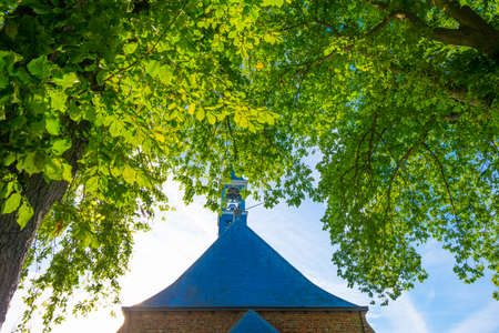 Trees and an old church in sunlight and shadow under a blue sky at sunrise in summer, Walcheren, Zeeland, the Netherlands, July, 2022の写真素材