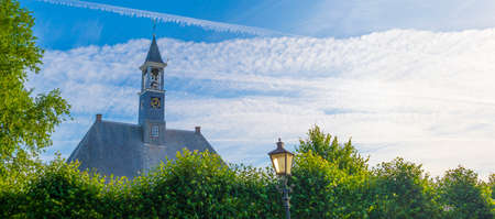 Trees and an old church in sunlight and shadow under a blue sky at sunrise in summer, Walcheren, Zeeland, the Netherlands, July, 2022の写真素材