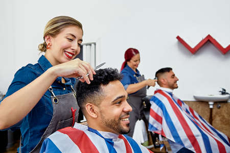 Two women hairdressers in the barbershop cutting the hair of customers. Everyone is happy