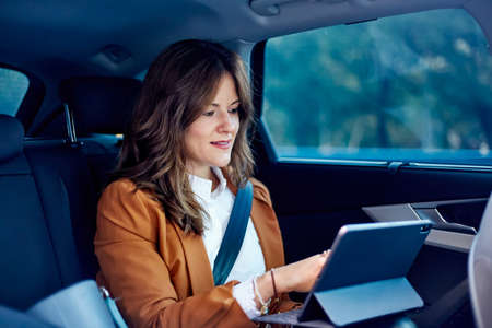 Caucasian woman working from the back seat of a car - Business woman using a laptopの写真素材