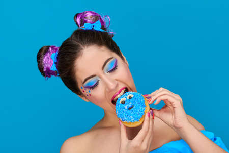 Pretty girl with red lips and hair up from eating a donuts, wearing colorful makeupの写真素材