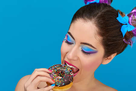 Pretty girl with red lips and hair up from eating a donuts, wearing colorful makeupの写真素材