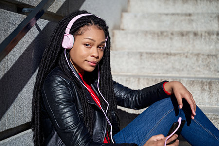 A portrait of a smiling African-American woman with a cell phone is chatting or listening to music on the streets of the city. The hair is braided into dreadlocks.の写真素材