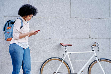 African American woman with a smart phone in her hand. She rides a bicycle through the city.