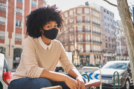 African American woman sitting on a bench. Latina woman with face mask . Concept of new normalityの写真素材