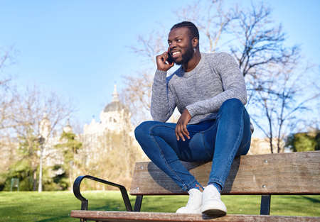 Happy black man talking on smart phone sitting in a park on a sunny day.の写真素材