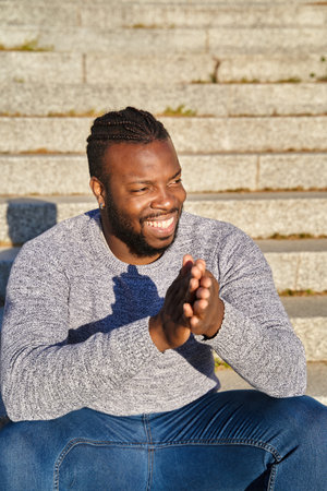 African American man sitting on the stairs smiling on a sunny day. Happy young Latino man. Concept...