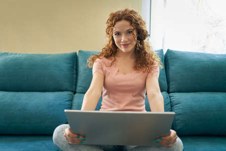 Smiling young woman using laptop, sitting on couch at home, beautiful girl shopping or chatting...