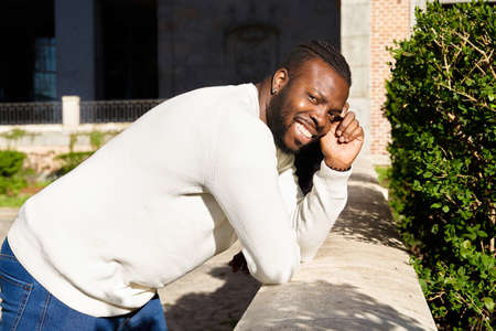 Young African American man smiling leaning against a wall, Happy Latino man.