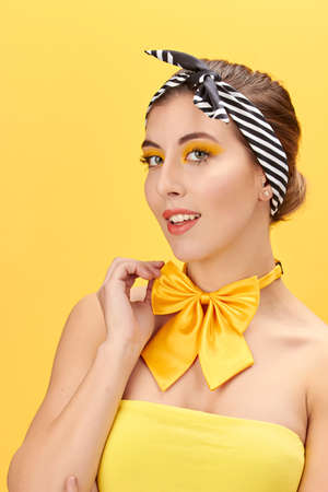 Pretty girl with yellow T-shirt, yellow neck bow, black headscarf and red lips, on yellow background.の写真素材
