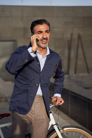 Adult male sitting talking on the phone with bicycle leaning against the wall. Ecological transport concept.の写真素材