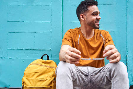 Happy young latino man sitting with sunglasses a backpack on one side. Resting from a walk in the...