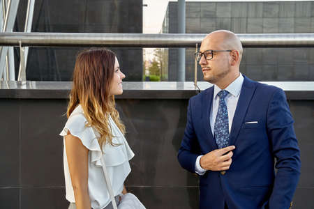 Self-confident man in suit and glasses standing near a modern building with a female colleague.の写真素材