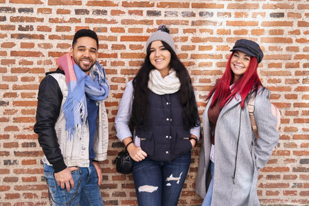 Smiling diverse stylish friends standing near brick wall