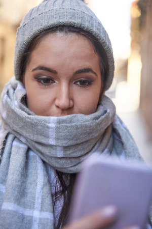 Happy young woman smiling while browsing smartphone on street