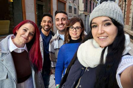 Positive multi-ethnic friends standing and smiling broadly as they self-portrait themselves on a...