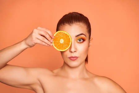 Closeup portrait of beautiful happy girl holding half of oranges near face, isolated on orange background. Concept of beauty and health care. High quality photoの写真素材