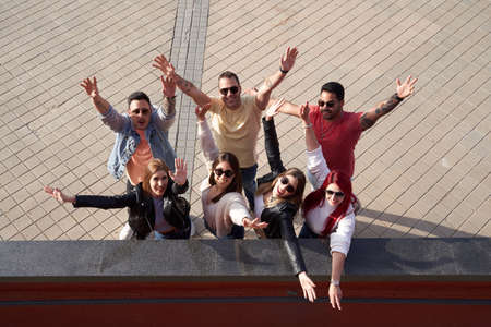From above group of cheerful young multiracial male and female friends in casual clothes raising...