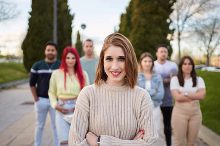 Confident woman looking at camera and smiling while standing with crossed arms in front of group of...