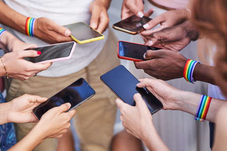Group of multiracial people with LGBT rainbow flag wristbands using their mobile phones. Diversity, LGBT, unity and technology concept.の写真素材