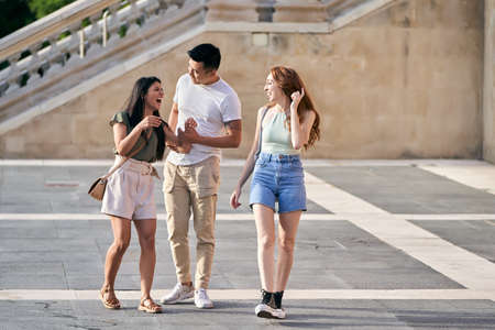 Three friends talking and laughing while walking outdoors together. Friendship and urban lifestyle...