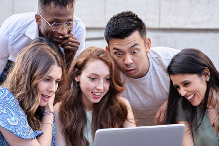 Group of multiracial people using a laptop computer together while sitting on stairs outdoors. Urban...