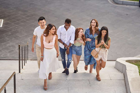 Group of multiracial friends laughing and chatting while walking up the stairs outdoors. Friends wearing LGBT flag wristbands. Diversity, friendship and LGBT concept.の写真素材