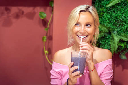 Joyful woman looking away and smiling while drinking a fresh smoothie in a cafe. Healthy lifestyle and beverages concept.の写真素材