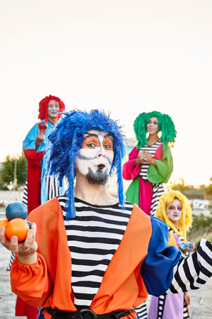 Male and female clowns in colorful costumes and wigs, looking at the camera holding crystal balls in...