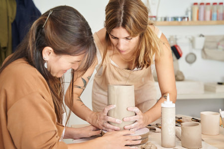 Two women working with clay in a pottery workshop. Craft, art and hobbies concept.の写真素材