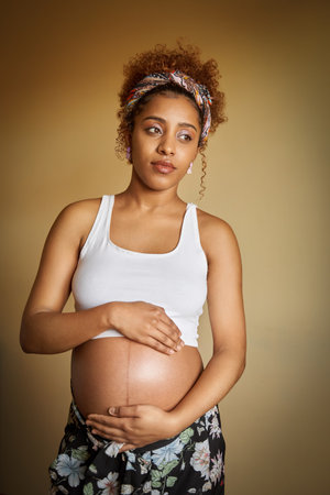 Pregnant woman holding her belly while standing on an isolated background. Pregnancy and maternity...