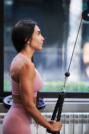 Fit brunette woman doing sport on a pulley at the gym. Healthy living concept