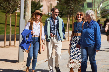 Four friends in their 60s strolling through a city square on a sunny day.の写真素材