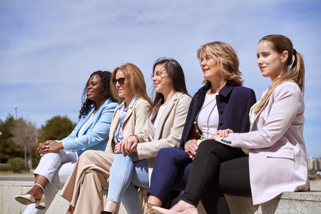 Group of businesswomen looking away while sitting on a bench outdoors. Business concept.の写真素材