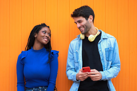 Multi-ethnic couple looking at each other while using headphones and mobile phone. Technology and...