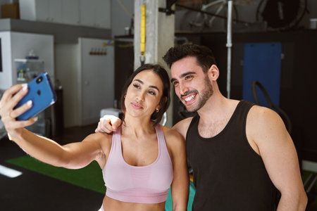 brunette fitness couple taking a selfie with their cell phone smiling after finishing their workout