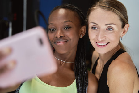 two fitness friends taking a happy selfie with their mobile phone after training at the gymの写真素材