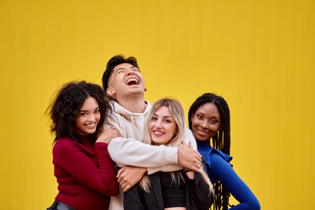 Happy multi-ethnic friends posing together in front of a yellow wall. Friendship concept.の写真素材