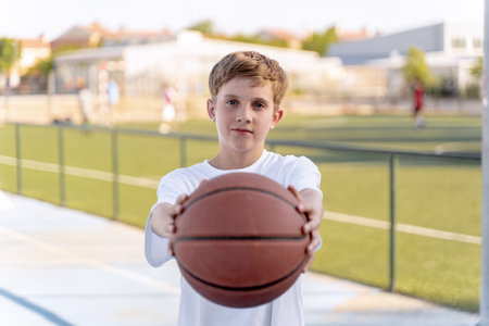 Teenage boy holding and showing basketball ball while posing outdoors. Sports concept.の写真素材